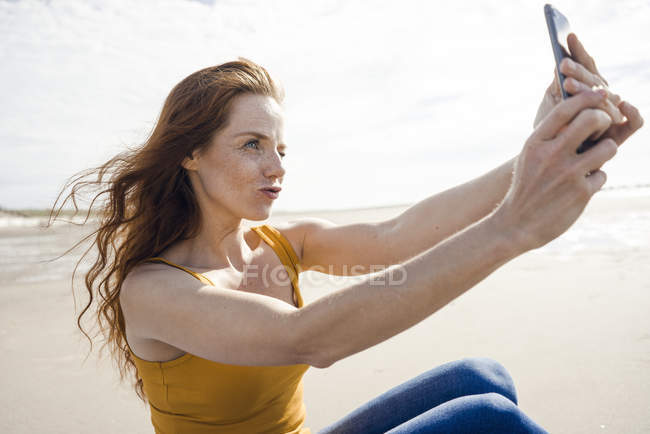 Руда жінка бере смартфон селфі на пляжі — стокове фото