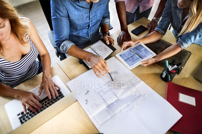 Колеги обговорюють план на столі в офісі — стокове фото