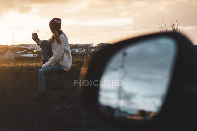 Ісландія, молода жінка з кавою, щоб піти на захід сонця, крило дзеркало — стокове фото