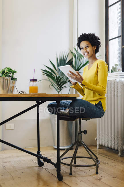 Молода афроамериканська жінка, яка сидить вдома і читає на цифровій дощечці. — стокове фото