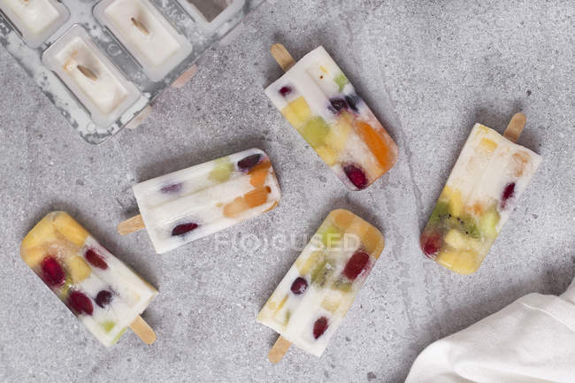 Homemade fruits and yogurt ice lollies on marble — Stock Photo