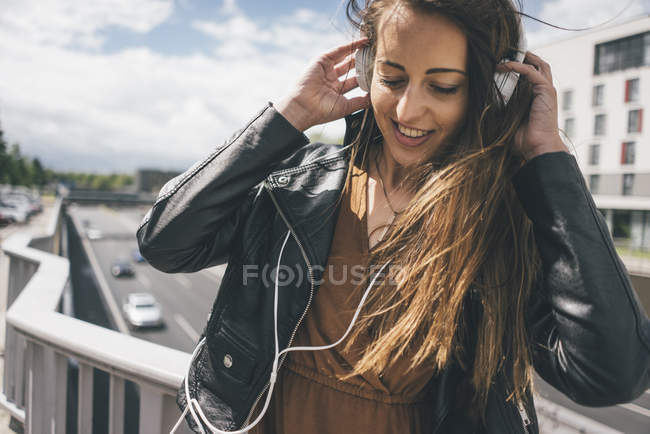 Jeune femme souriante écoutant de la musique sur un pont autoroutier — Photo de stock
