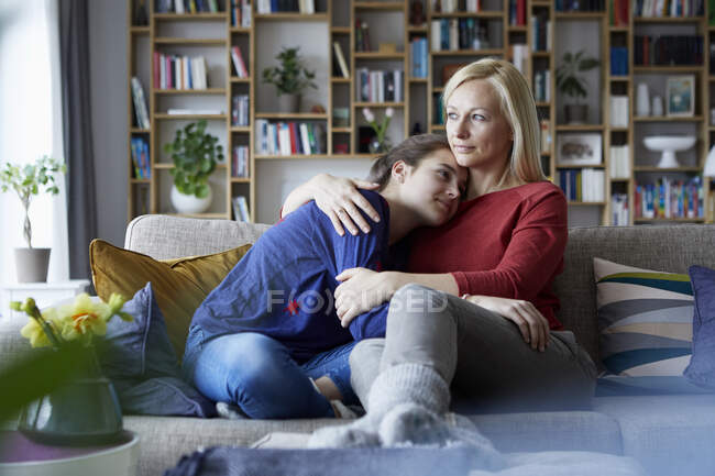 Мать и дочь-подросток сидят на диване с руками вокруг — стоковое фото