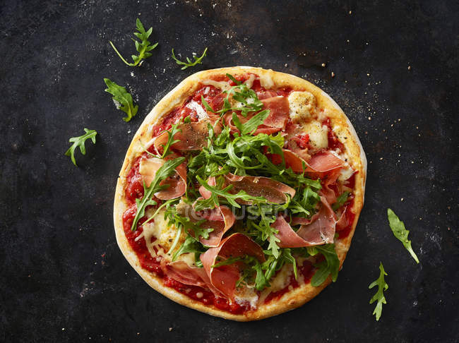 Pizza with ham and rocket on dark ground — Stock Photo