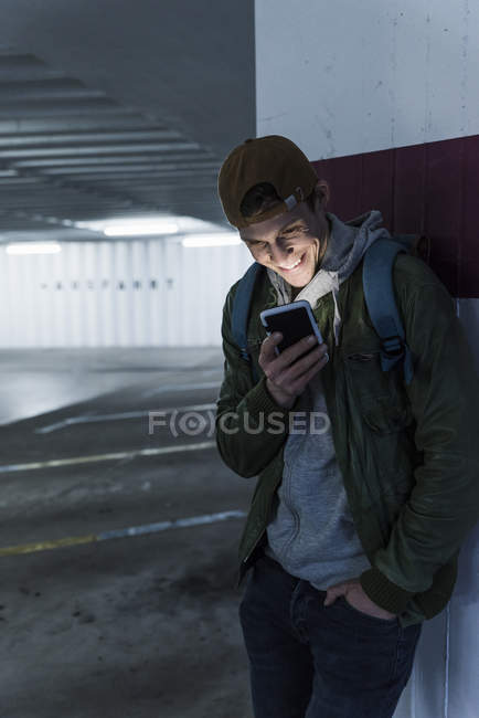 Hombre sonriente mirando brillante teléfono inteligente en el garaje de estacionamiento - foto de stock