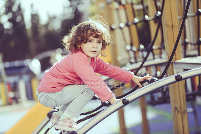 Ritratto di bambina accovacciata su telaio da arrampicata al parco giochi — Foto stock