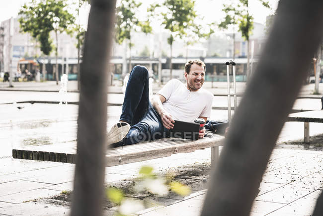 Улыбающийся мужчина лежит на скамейке с табличкой — стоковое фото