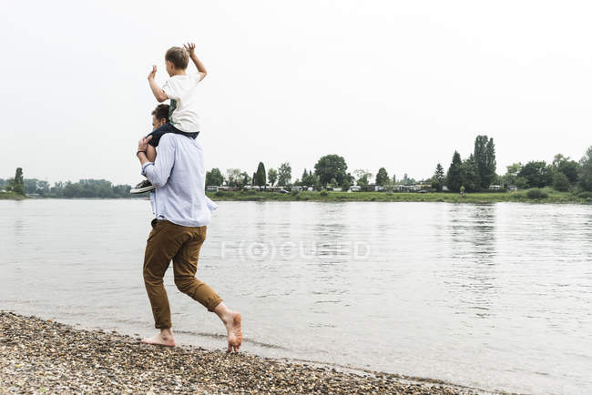 Father carrying son on shoulders at the riverside — Stock Photo