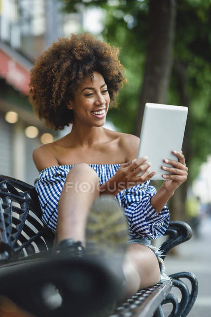 Портрет сміху молодої жінки, що сидить на лавці, використовуючи планшет — стокове фото