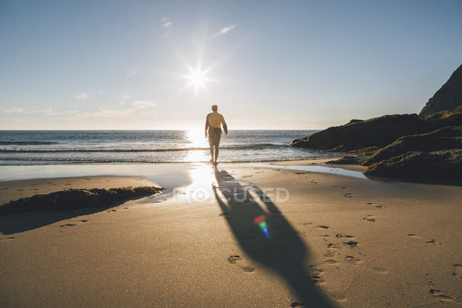 Norway, Lofoten, Moskenesoy, Man walking into the sun at Kvalvika Beach — Stock Photo
