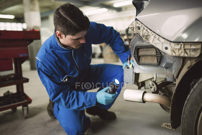 Mecânico inspecionar um carro com uma tocha em uma oficina — Fotografia de Stock
