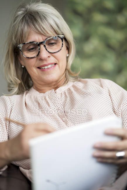 Smiling mature woman drawing on sketchbook — Stock Photo