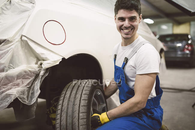 Portrait of smiling mechanic changing car tyre in his workshop — Stock Photo