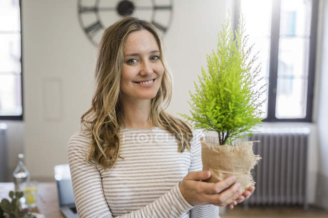 Портрет улыбающейся женщины, держащей растение дома — стоковое фото