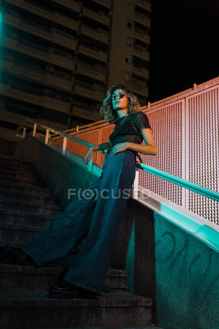 Mujer joven con estilo en la noche en la ciudad, con gafas de sol - foto de stock
