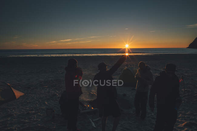 Norway, Lofoten, Moskenesoy, Young men standing at Kvalvika Beach at sunset — Stock Photo