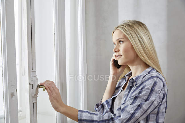 Білява жінка по телефону, що дивиться з вікна — стокове фото