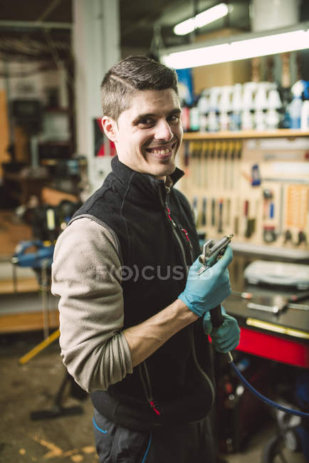 Retrato de un mecánico sonriente en su taller - foto de stock