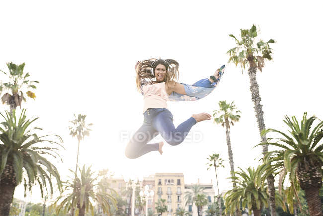 Spagna, Barcellona, ritratto di una giovane donna sorridente con le cuffie che salta in aria — Foto stock