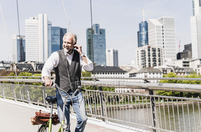 Усміхнений зрілий чоловік з навушниками і велосипедний перехідний міст у місті — стокове фото