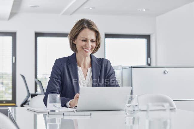 Lächelnde Geschäftsfrau mit Laptop am Schreibtisch im Büro — Stockfoto