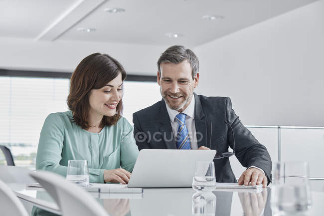 Empresario y mujer de negocios teniendo una reunión en la oficina con el ordenador portátil - foto de stock