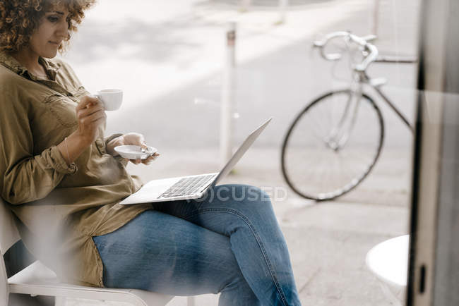 Жінка працює в кафе, п'є каву, використовуючи ноутбук — стокове фото
