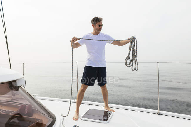 Hombre maduro de pie en catamarán, cuerda enrollable - foto de stock
