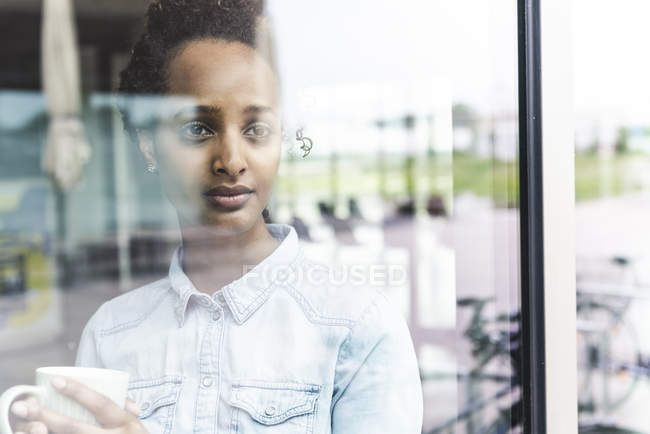 Portrait of young businesswoman looking out of window, holding coffee cup — Stock Photo