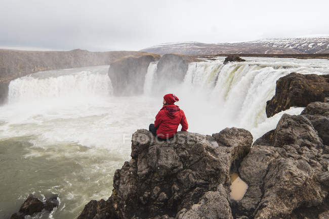 Islandia, hombre sentado en la cascada Godafoss - foto de stock