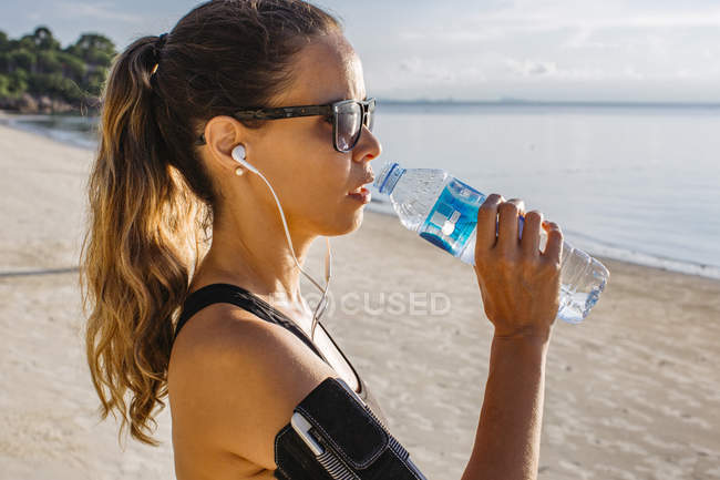 Thailand, Koh Phangan, Sportive woman drinking water on the beach — Stock Photo