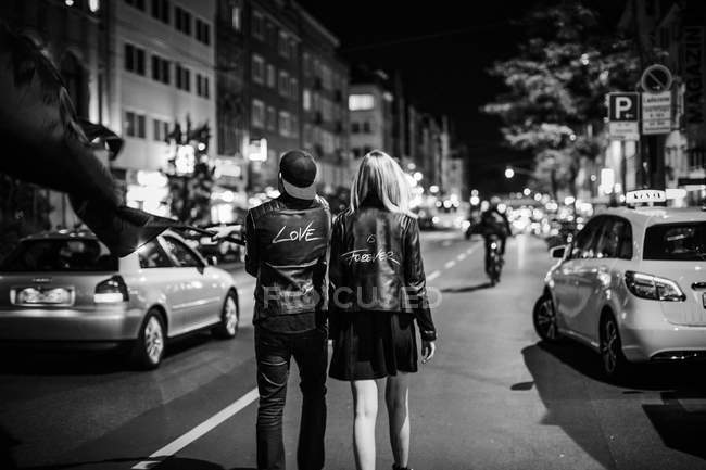 Vista trasera de pareja joven con bandera negra caminando por la calle por  la noche — tema, Escena urbana - Stock Photo | #265349776