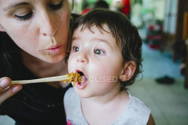 Thailand, Chiang Mai, Mother feeding her daughter with Pad Thai, using chopsticks — Stock Photo
