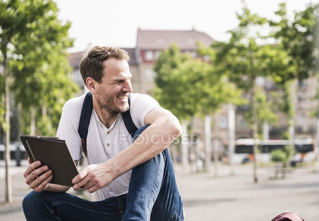 Uomo sorridente seduto all'aperto con tablet — Foto stock