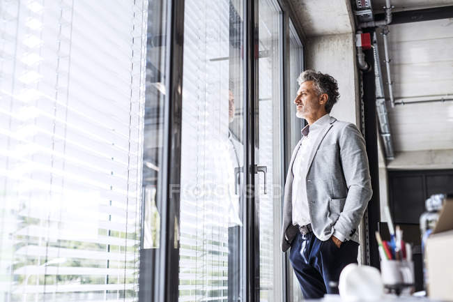 Reifer Geschäftsmann steht im Büro und schaut aus dem Fenster — Stockfoto