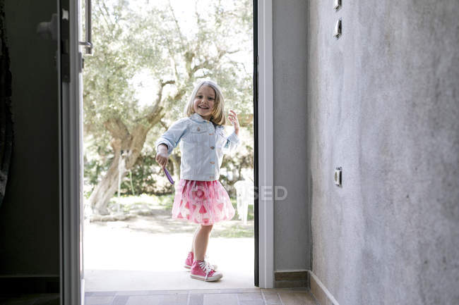 Portrait of laughing little girl standing in front of open entry door — Stock Photo