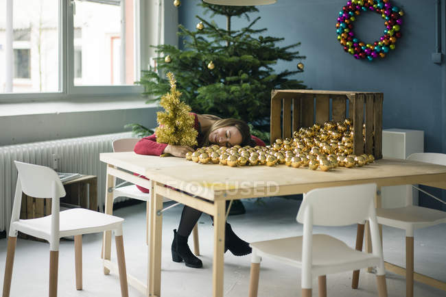 Woman sitting at table with many golden Christmas baubles — Stock Photo