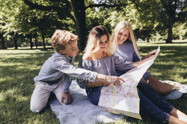 Two young women and a boy looking at map in a park — Stock Photo