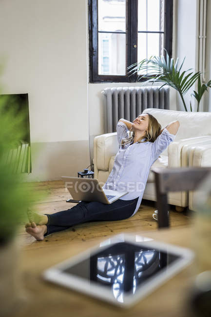 Femme souriante avec ordinateur portable à la maison penché en arrière — Photo de stock