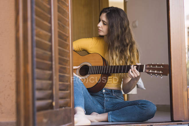 Jeune femme assise par terre à la maison jouant de la guitare — Photo de stock