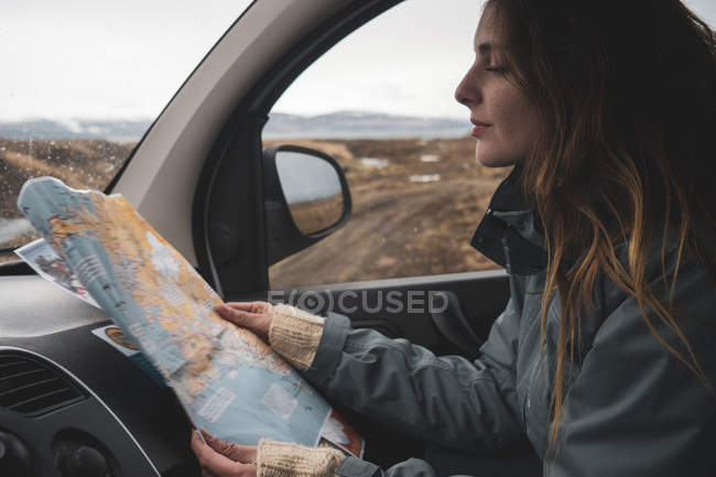Islandia, mujer joven en coche mirando el mapa - foto de stock