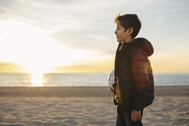 Garçon tenant ballon de football sur la plage au coucher du soleil — Photo de stock