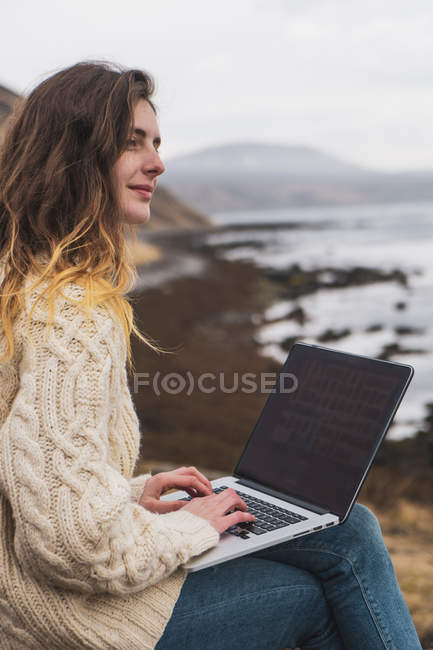 Islandia, mujer usando laptop en la costa - foto de stock