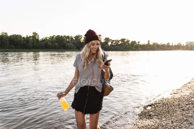 Jeune femme marchant pieds nus sur la rivière, écouteurs et smartphone — Photo de stock
