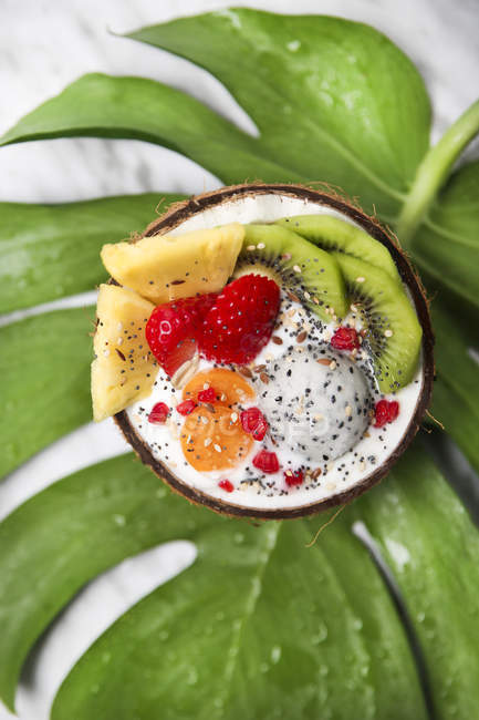 Coconut bowl with variuos fruits, natural yoghurt and seeds on leaf — Stock Photo