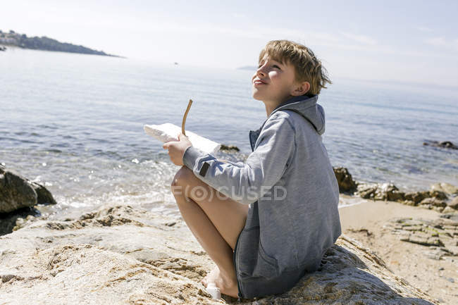 Ragazzo seduto al mare con auto-fatto barca giocattolo — Foto stock