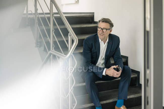 Sorridente uomo d'affari maturo con cellulare seduto sulle scale — Foto stock