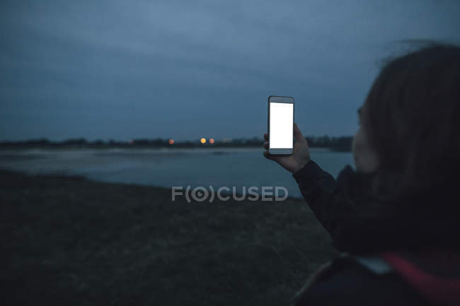 France, Brittany, Landeda, woman with cell phone at the coast at dusk — Stock Photo