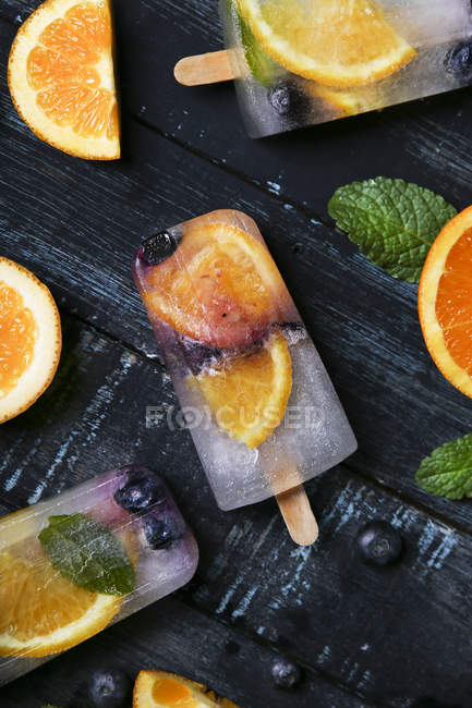 Popsicles de désintoxication maison aux myrtilles, tranches d'orange et feuilles de menthe sur bois noir — Photo de stock