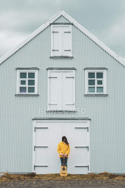 Islandia, mujer con guitarra de pie en casa - foto de stock